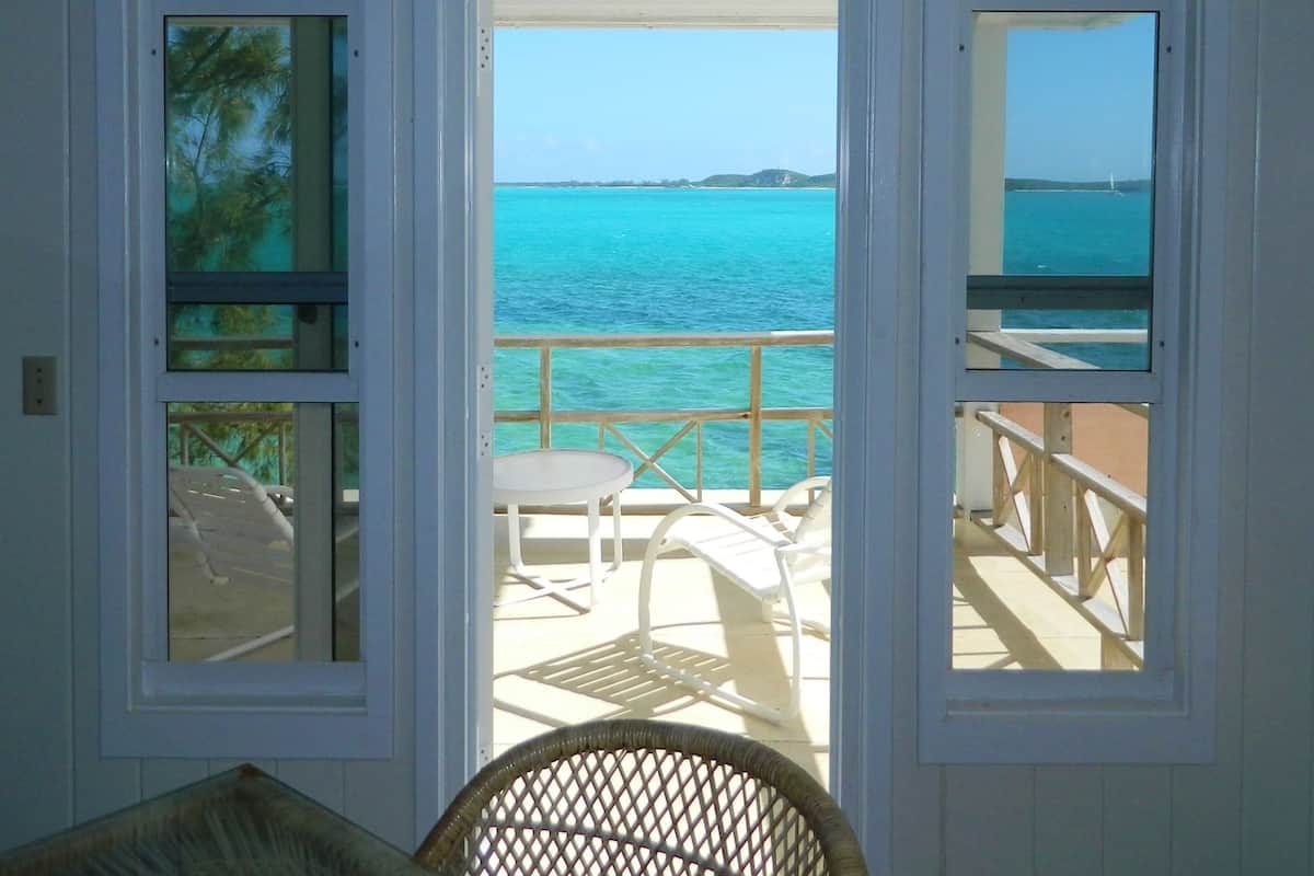 A room with a view of the sea through open doors. There is a chair and a table in the room.