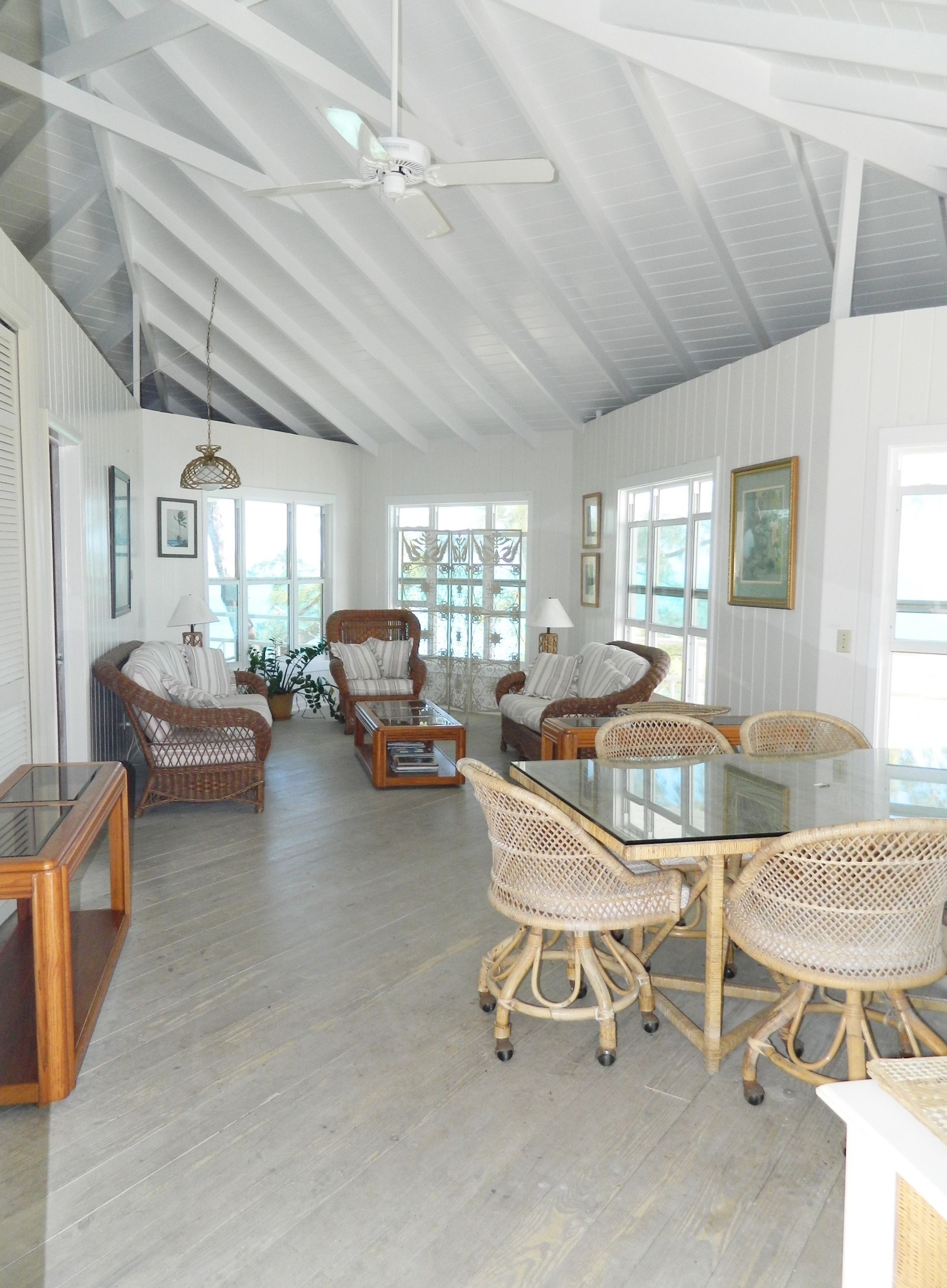 A spacious living room with high ceilings, a large dining table surrounded by wicker chairs, and a ceiling fan.