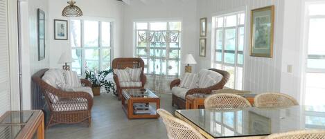 A spacious living room with high ceilings, a large dining table surrounded by wicker chairs, and a ceiling fan.