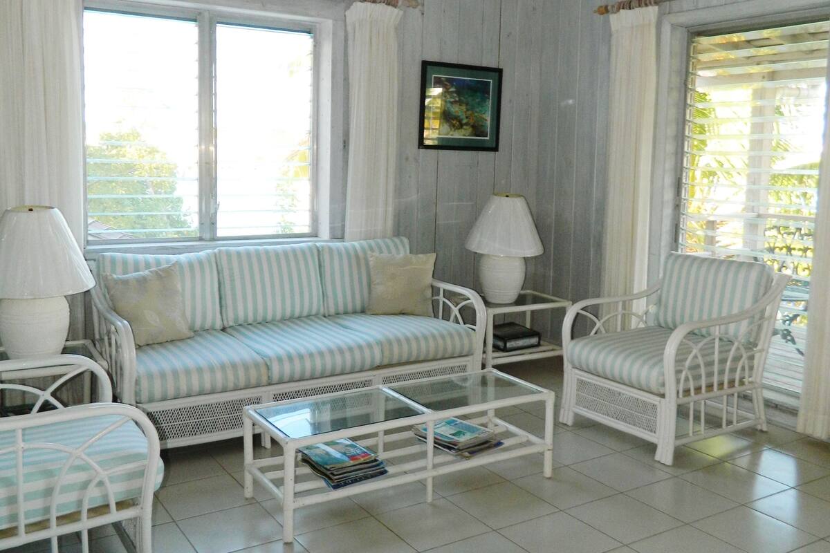 A room with a white sofa, two armchairs, a coffee table, and a ceiling fan.