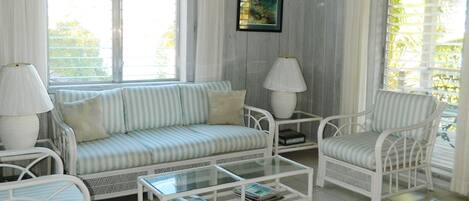 Une pièce avec un canapé blanc, deux fauteuils, une table basse et un ventilateur de plafond.