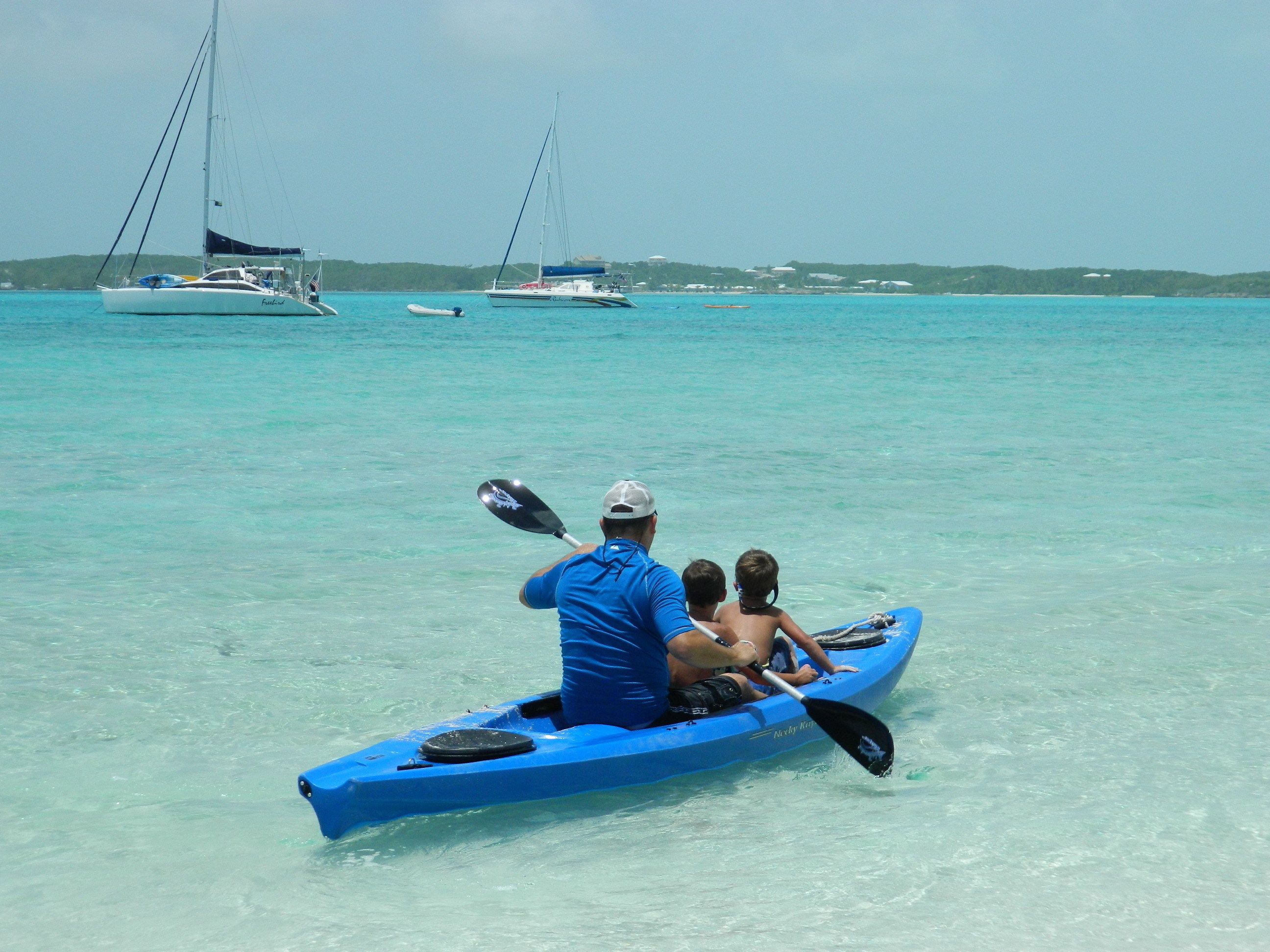 A clear turquoise sea with a man paddling a blue kayak.