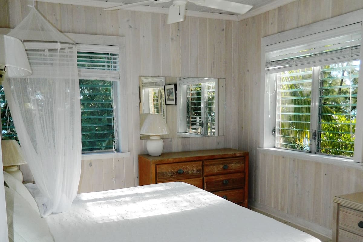 A bedroom with a bed, a wooden dresser, a mirror, and a ceiling fan.