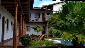 Un patio con piscina, sillas de madera y plantas en macetas.