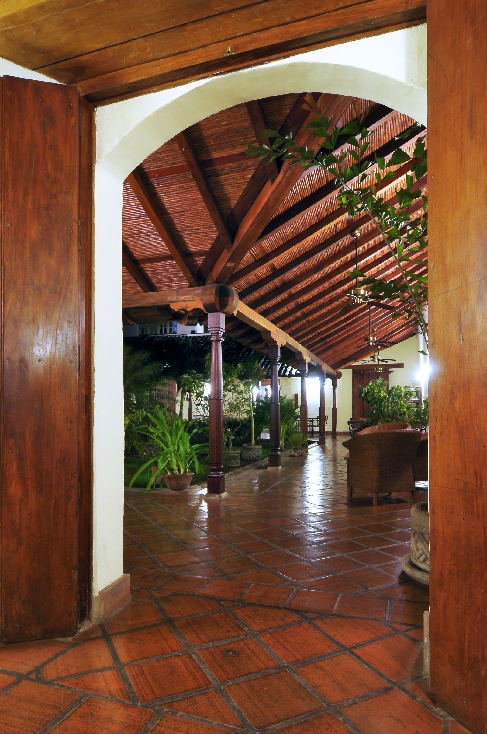 An indoor covered area with a tiled floor, wooden columns, and a ceiling with wooden beams.