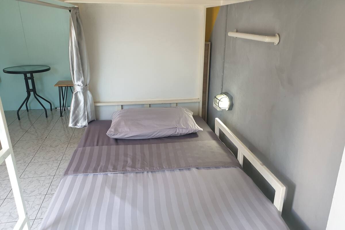 Una cama individual con ropa de cama a rayas, una mesita de noche, una silla y un aplique de pared.
