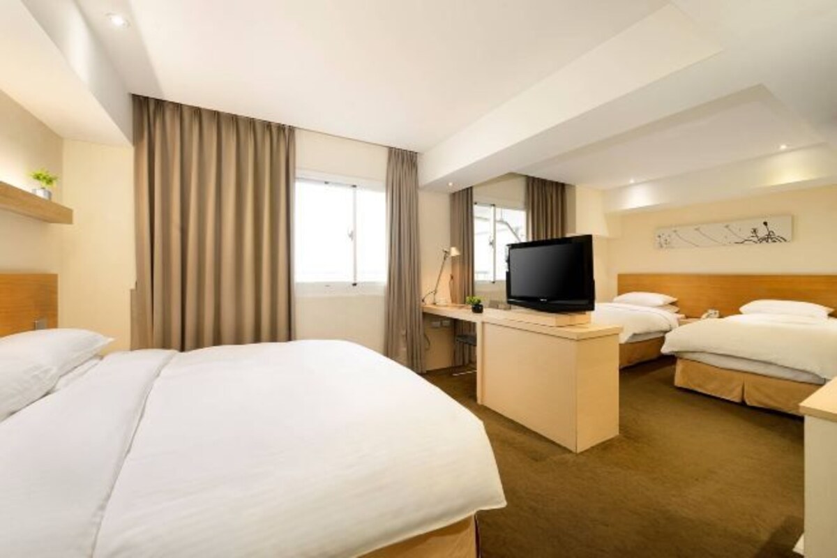 A hotel room with two beds, a desk with a TV, and a window with curtains.