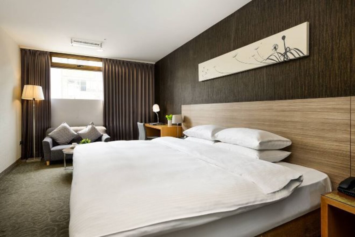 A hotel room with a large bed, a desk, a chair, a lamp, and a painting on the wall.