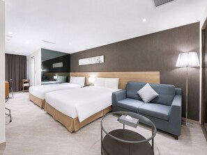 A hotel room with two beds, a sofa, a glass coffee table, and a lamp. - Beacon Hotel (Taichung)