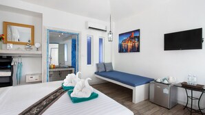 A hotel room with a bed, a small seating area, a TV, a refrigerator, and a window with a view of a cityscape.