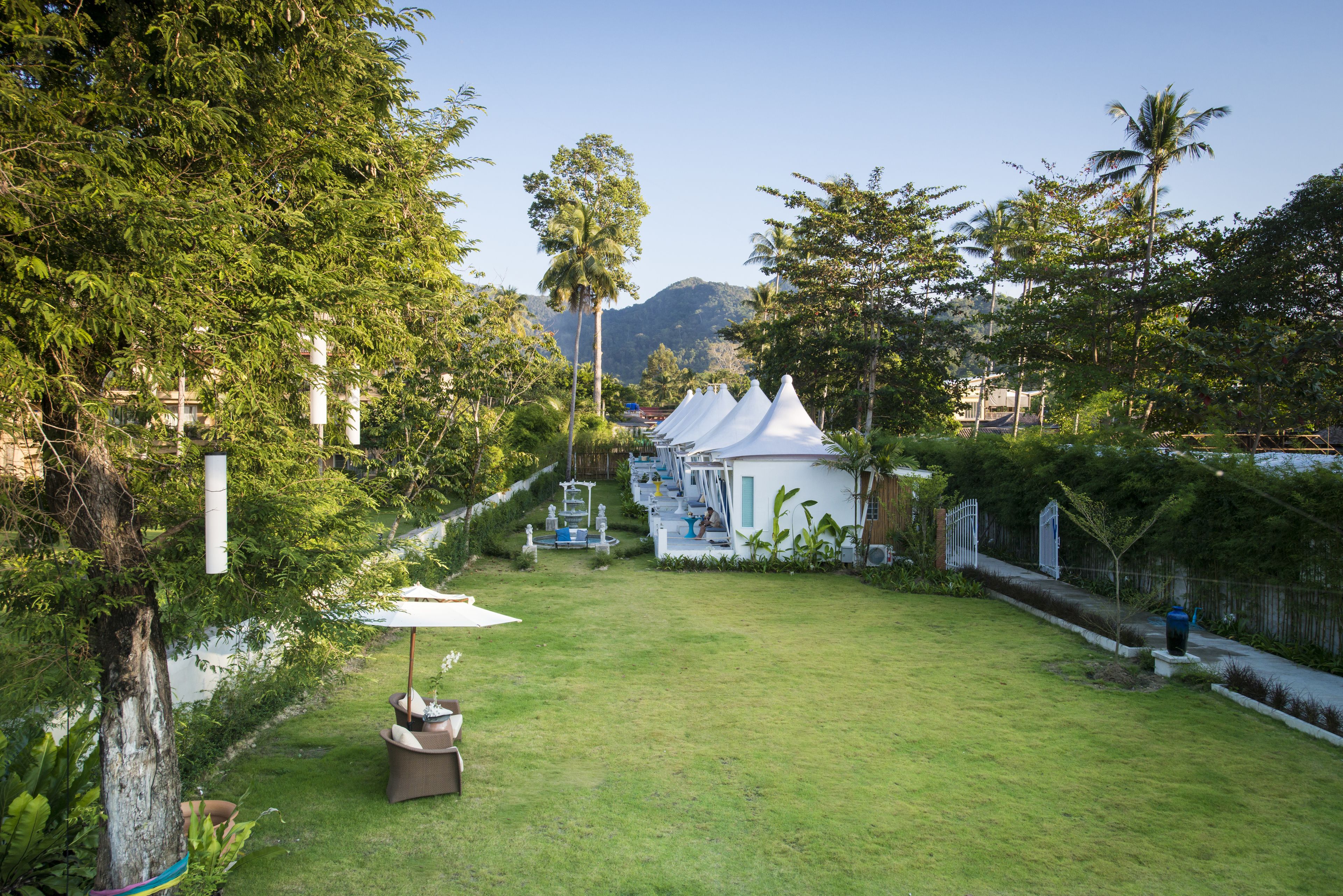 A well-maintained garden with a lawn, white tents, and a dining area with tables and chairs.