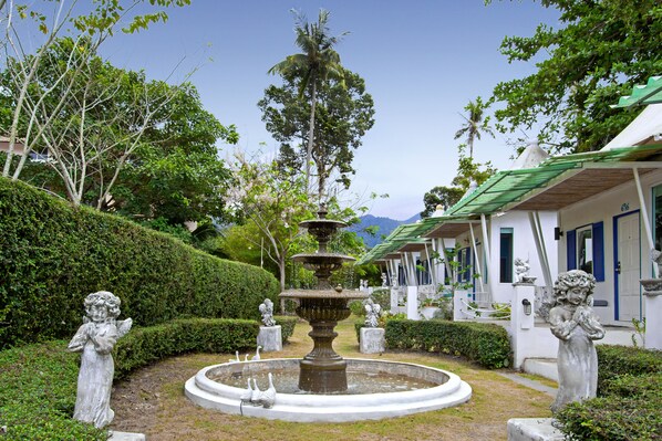 Un jardín con una fuente, estatuas y un edificio con contraventanas azules.