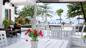 An outdoor seating area with white tables and chairs, a fan, and a potted plant with red flowers.