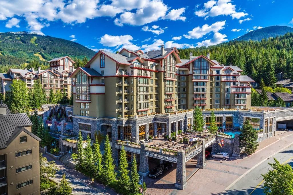Un hôtel à plusieurs étages, doté d’une façade en pierre, de balcons, et avec une station de ski en arrière-plan.