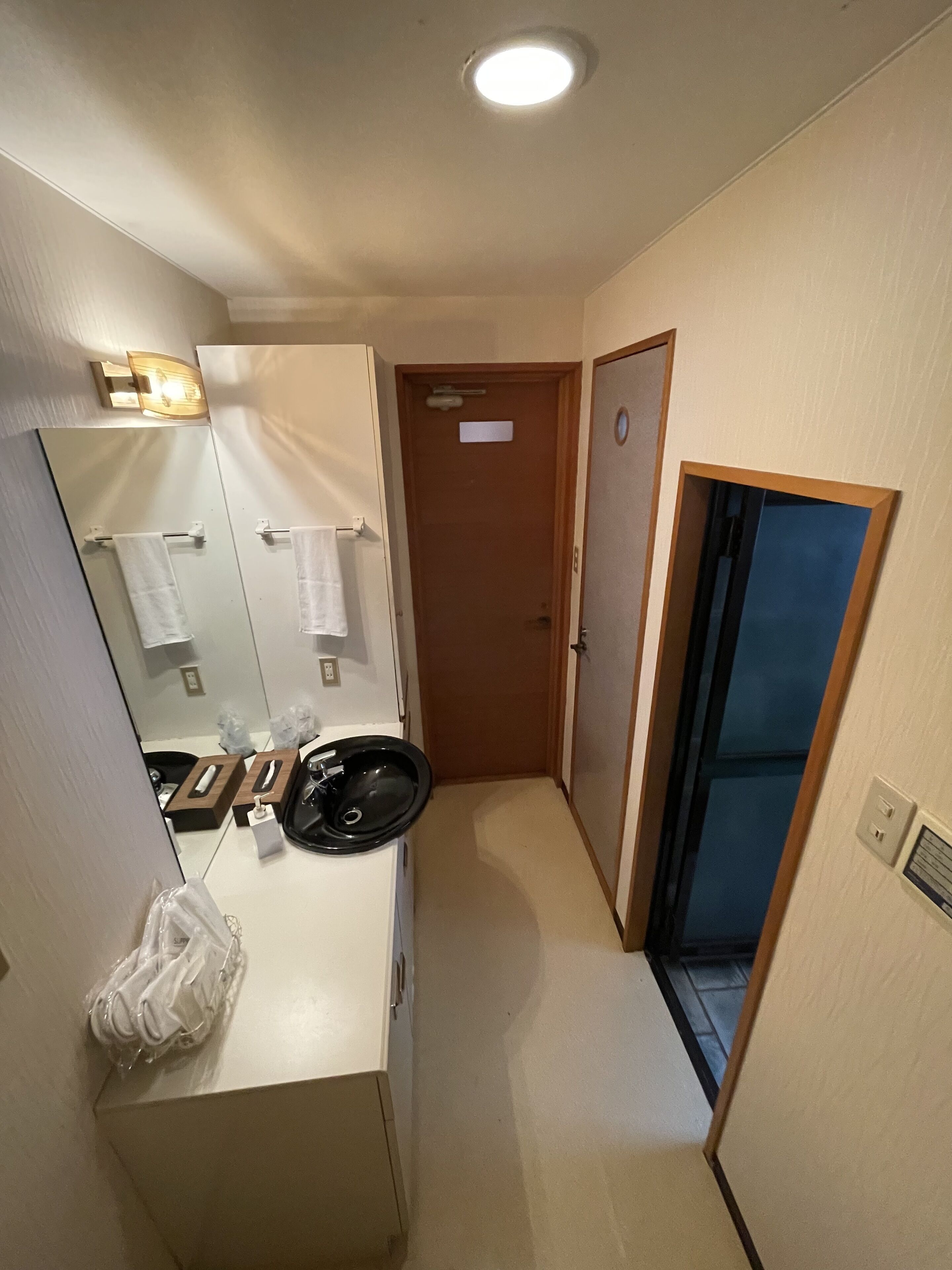 A narrow hallway with a sink, mirror, and a door leading to another room.