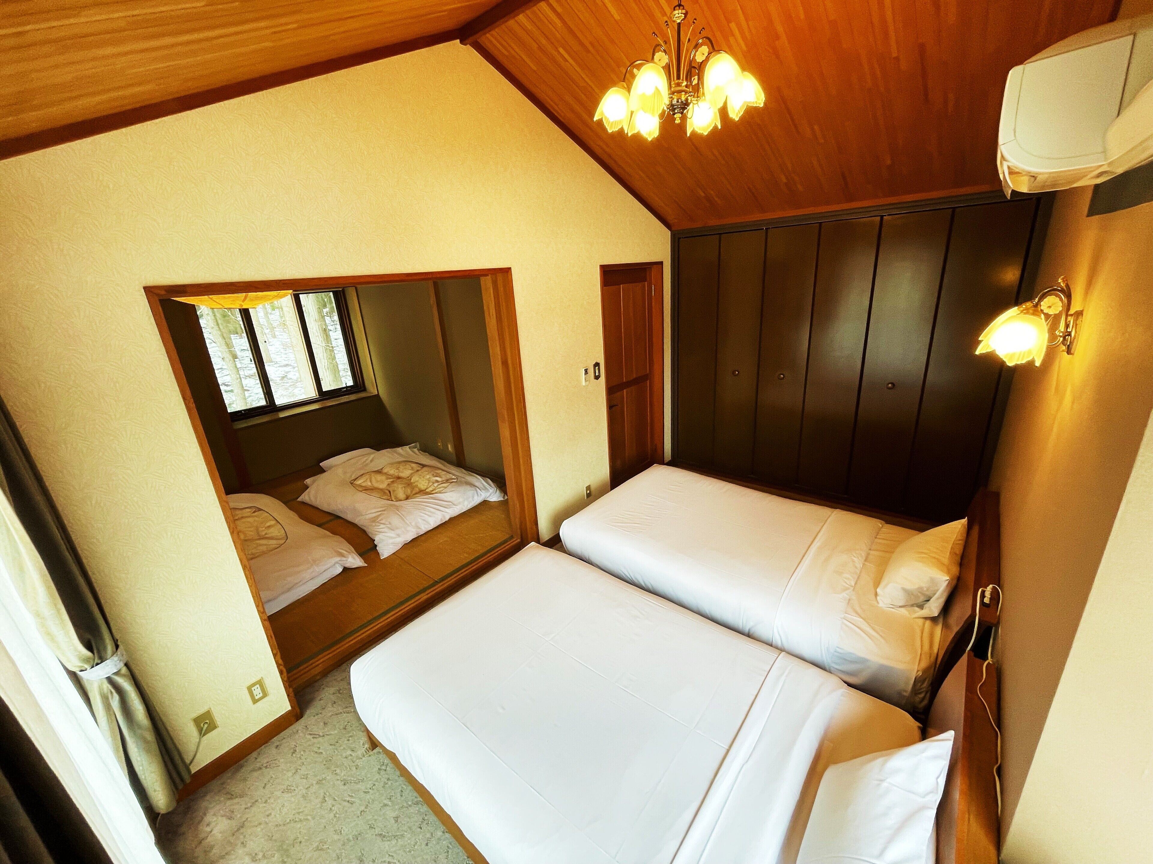 Un dormitorio con dos camas, techo de madera, un espejo y una ventana.