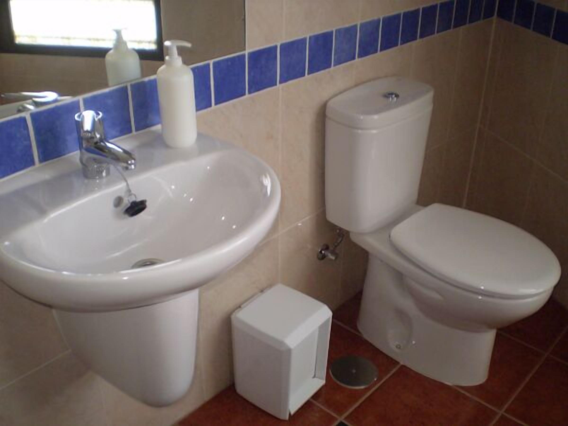 Un bany amb un lavabo, un vàter i una petita caixa blanca, probablement un dosificador de sabó, a terra.