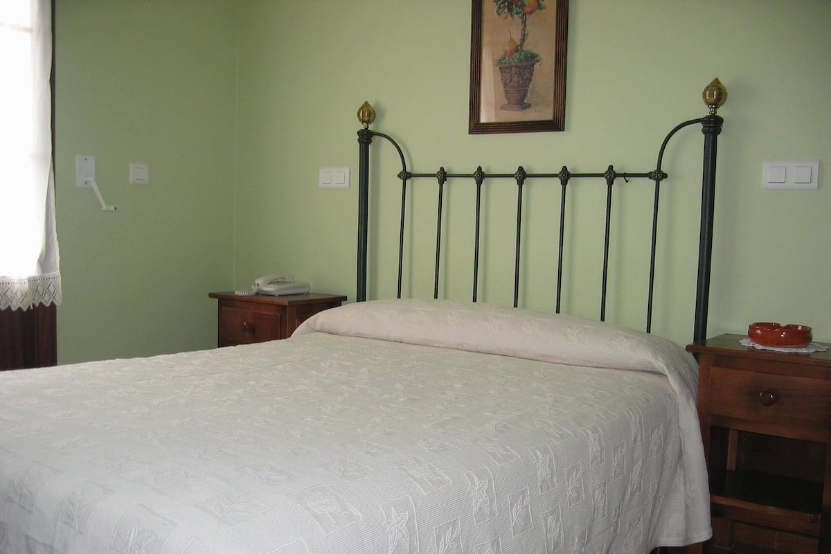 A bedroom with a bed, a nightstand, a bedside table, a lamp, and a wall-mounted painting.
