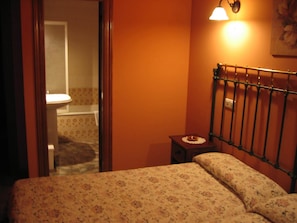 A bedroom with a bed, a nightstand, a mirror, and a bathroom visible through an open door. - Centro de Turismo Rural Lajafriz (Fonfria)