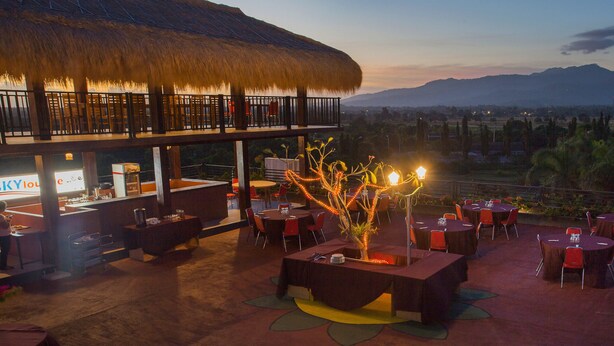 An outdoor dining area with tables and chairs, a bar, and a thatched roof structure.
