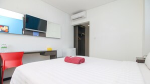 A hotel room with a bed, a desk, a chair, a TV, and an air conditioning unit.