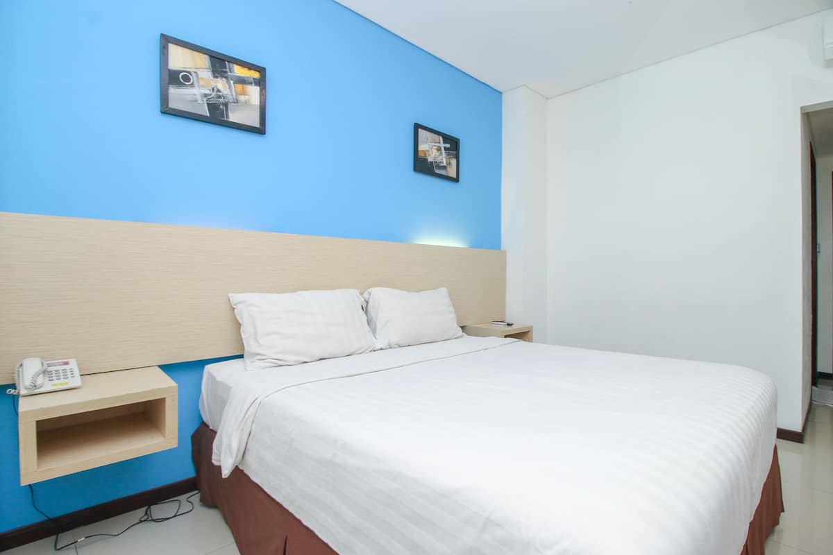 A hotel room with a bed, a bedside table with a phone, and two framed pictures on the wall.