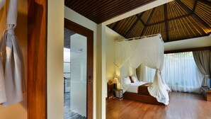Un dormitorio con piso de madera, cama con dosel, mesita de noche con lámpara y vistas al exterior a través de amplias ventanas.