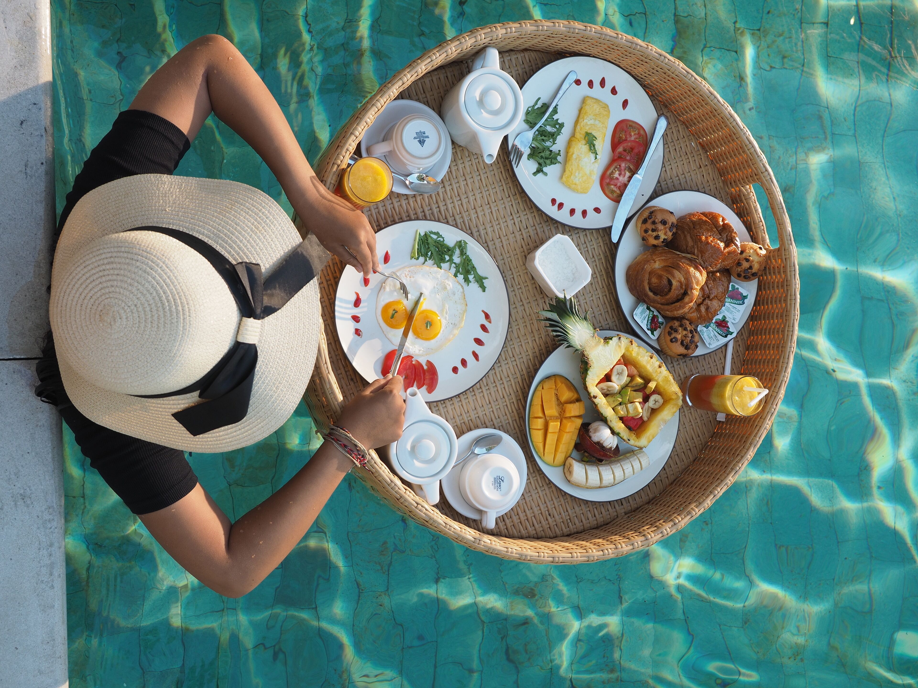 Una persona cenando junto a una piscina, con una bandeja que contiene comida y bebidas.