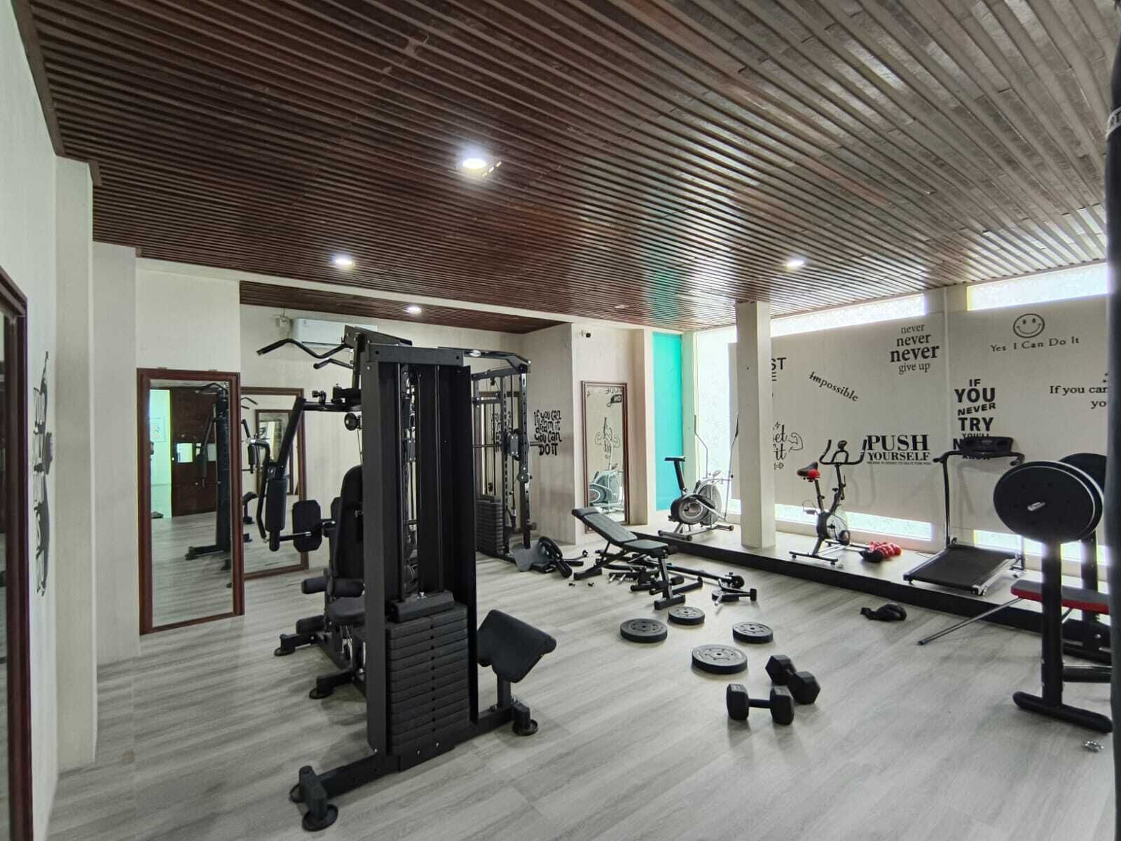 A gym with various exercise equipment, motivational wall quotes, and a wooden ceiling.