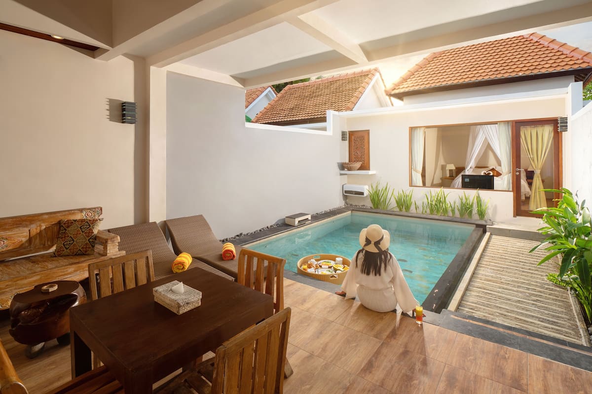 Zona junto a la piscina con una mesa, sillas y una persona sentada.