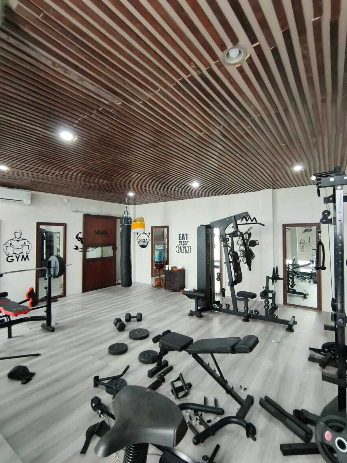 Ein Fitnessraum mit unterschiedlichen Trainingsgeräten, einer Holzbalkendecke und motivierenden Wandbildern.