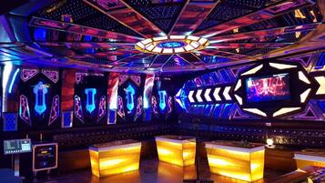 A modern, brightly lit control room with hexagonal panels, a central circular light fixture, and a large screen displaying a performance.