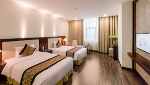 Une chambre d’hôtel avec deux lits, un bureau, une chaise, une petite table avec un vase et une grande fenêtre avec des rideaux.