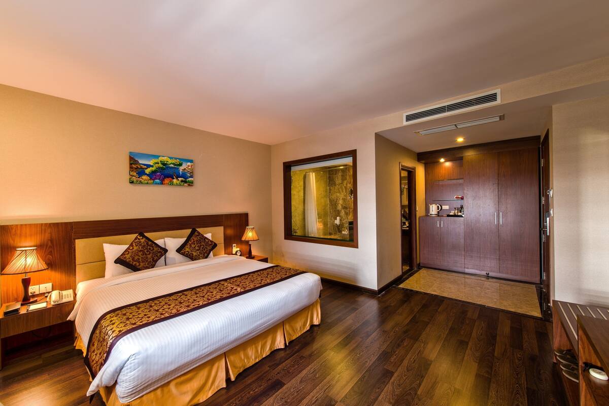 Ein Hotelzimmer mit einem großen Bett, einem Holzkopfstück, Nachttischlampen, einem Bild an der Wand und Blick auf den Flur.