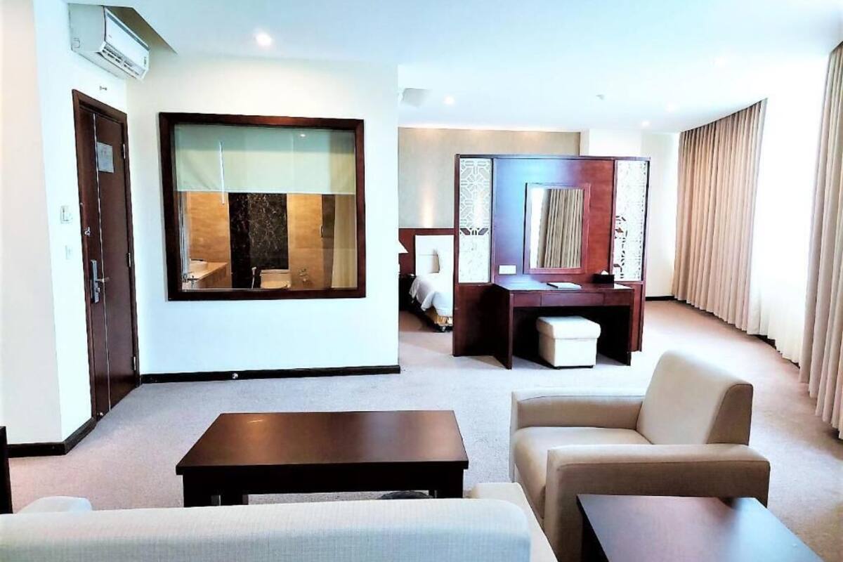 Ein modernes Hotelzimmer mit Wohnbereich, Schreibtisch, Sofa und großem Fenster.