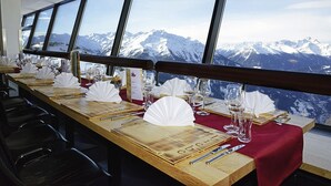 A dining table set with white tablecloths, silverware, and wine glasses, overlooking a mountain landscape. - Venet Gipfelhütte (Zams)