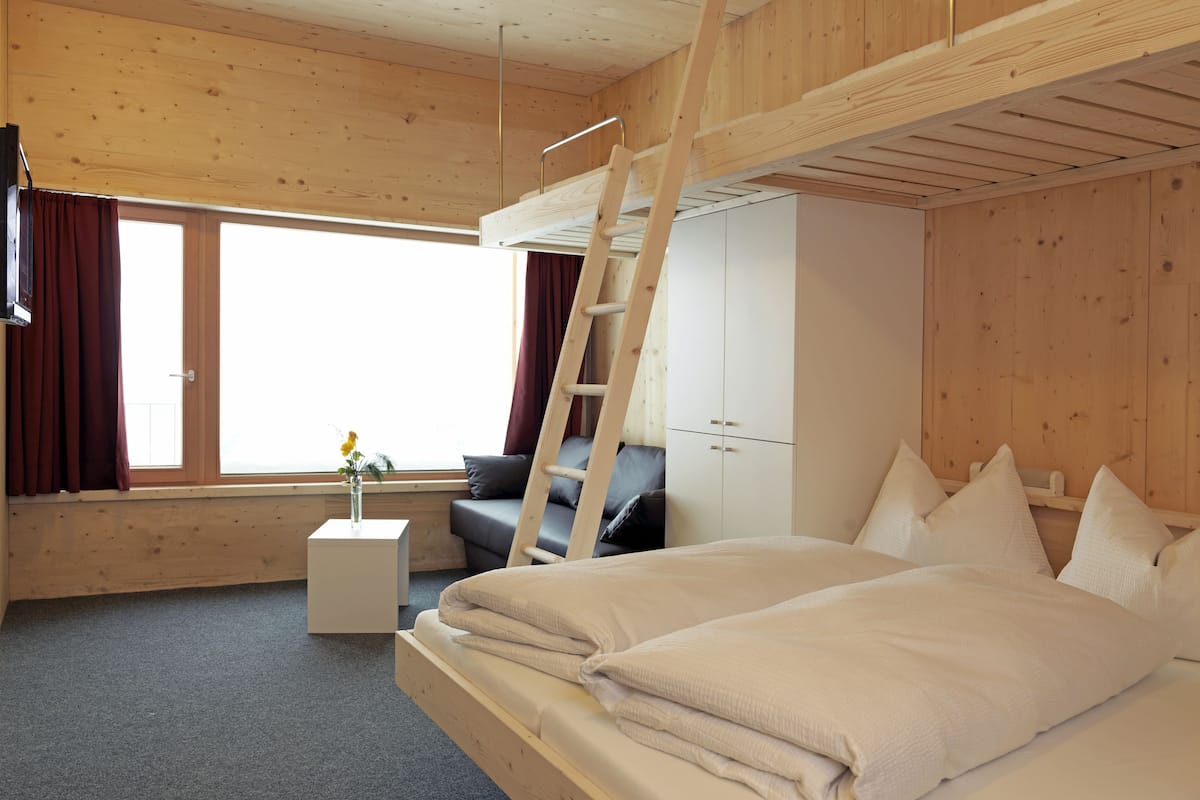 A room with a bunk bed, a small bedside table, a wardrobe, and a window with curtains.