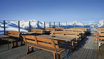 Eine Holzterrasse mit Picknicktischen und Bänken mit Blick auf ein verschneites Gebirge.