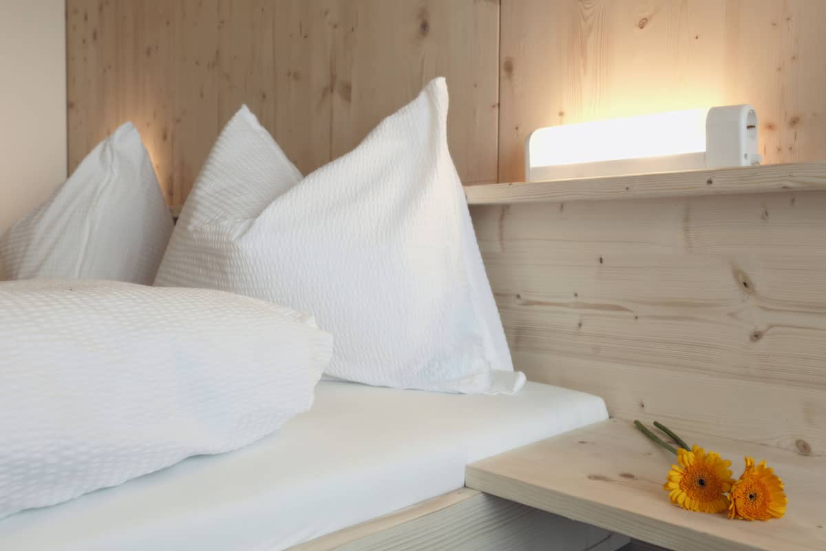 A bed with white bedding and pillows, a wooden headboard, and a bedside table with two yellow flowers.