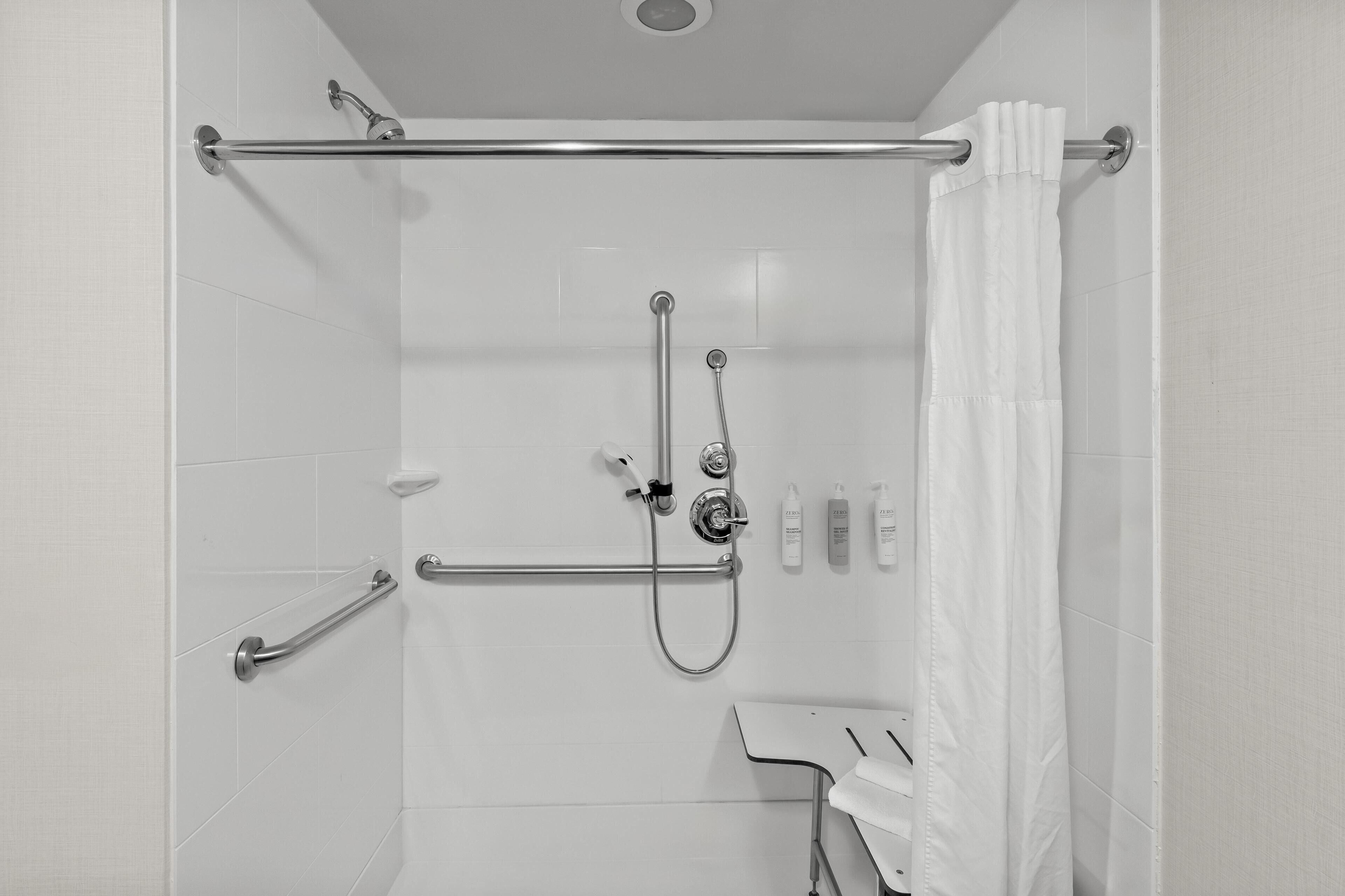 A shower with a grab bar, a handheld showerhead, and a towel rack.