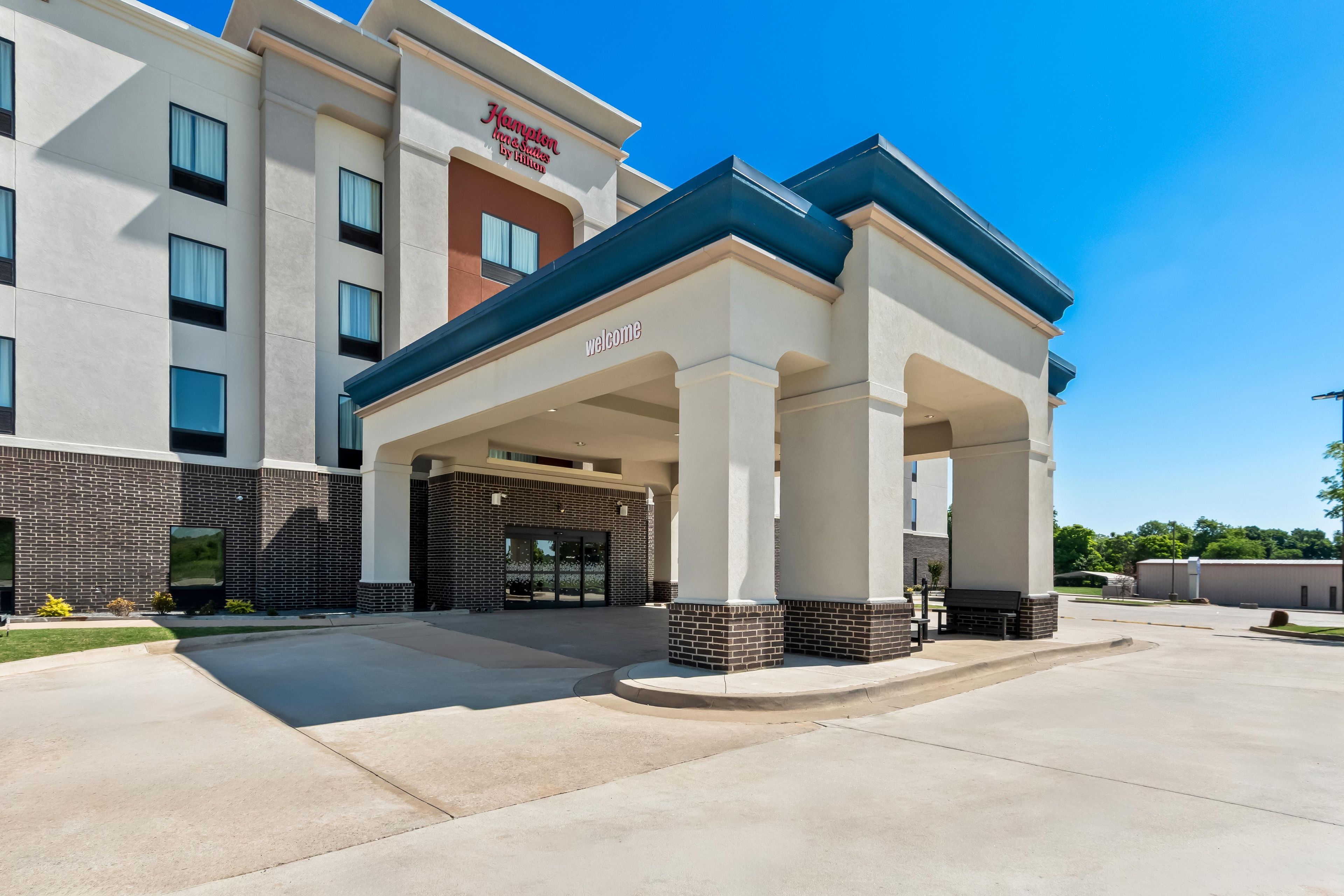 A hotel entrance with a covered walkway, columns, and a 'Welcome' sign.