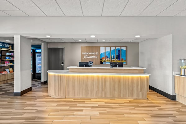 A reception desk with a 'Welcome to Hampton' sign, a cityscape mural, and a coffee machine.