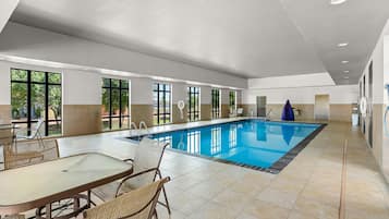 Un área amplia de piscina interior con una piscina larga, suelo de baldosas y sillas de mimbre.