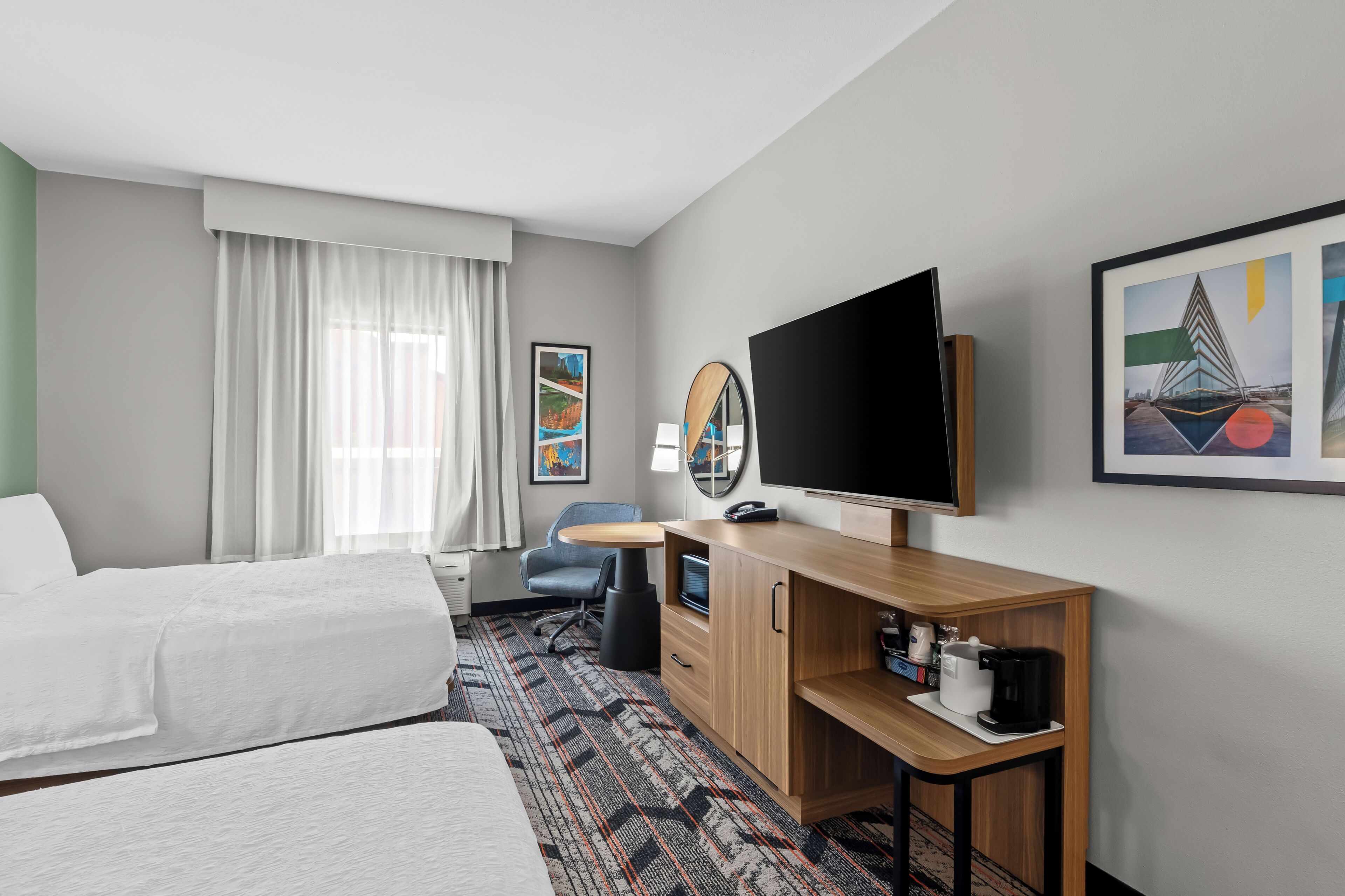 A hotel room with a bed, a desk, a television, a coffee maker, and artwork on the walls.