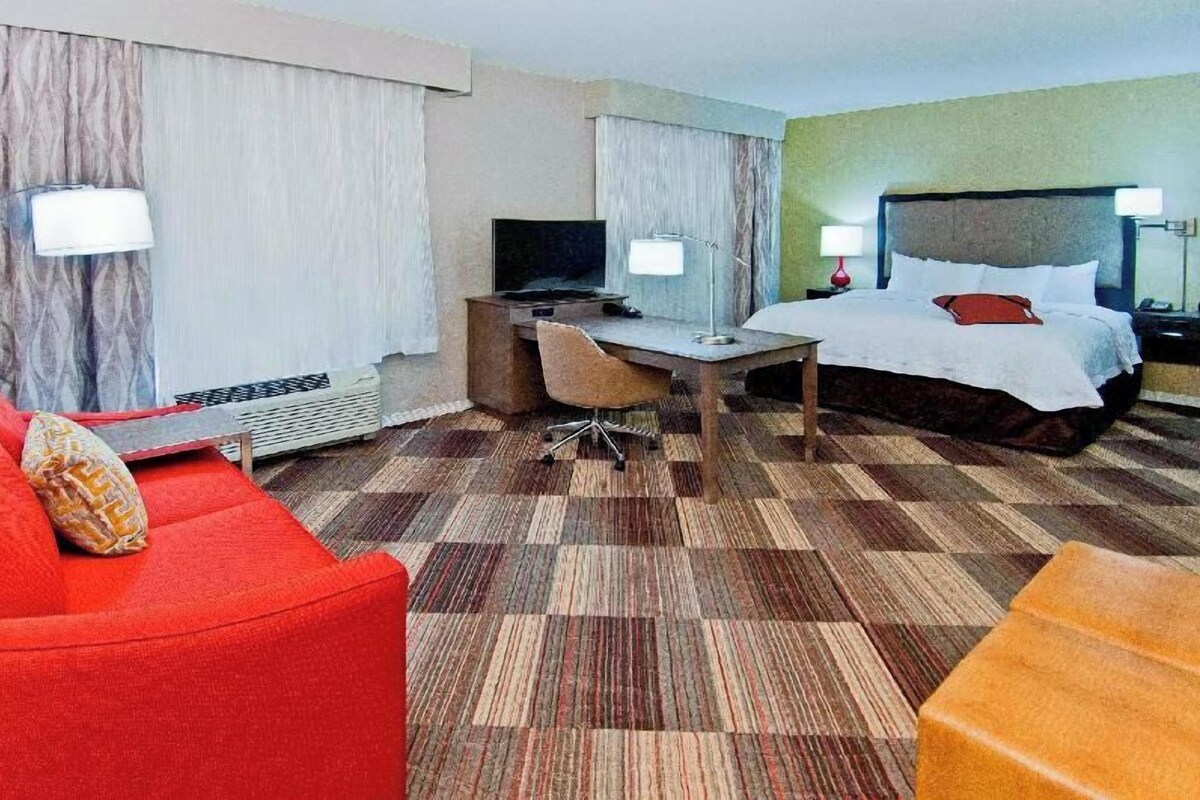 A hotel room with a bed, desk, chair, and a red sofa.
