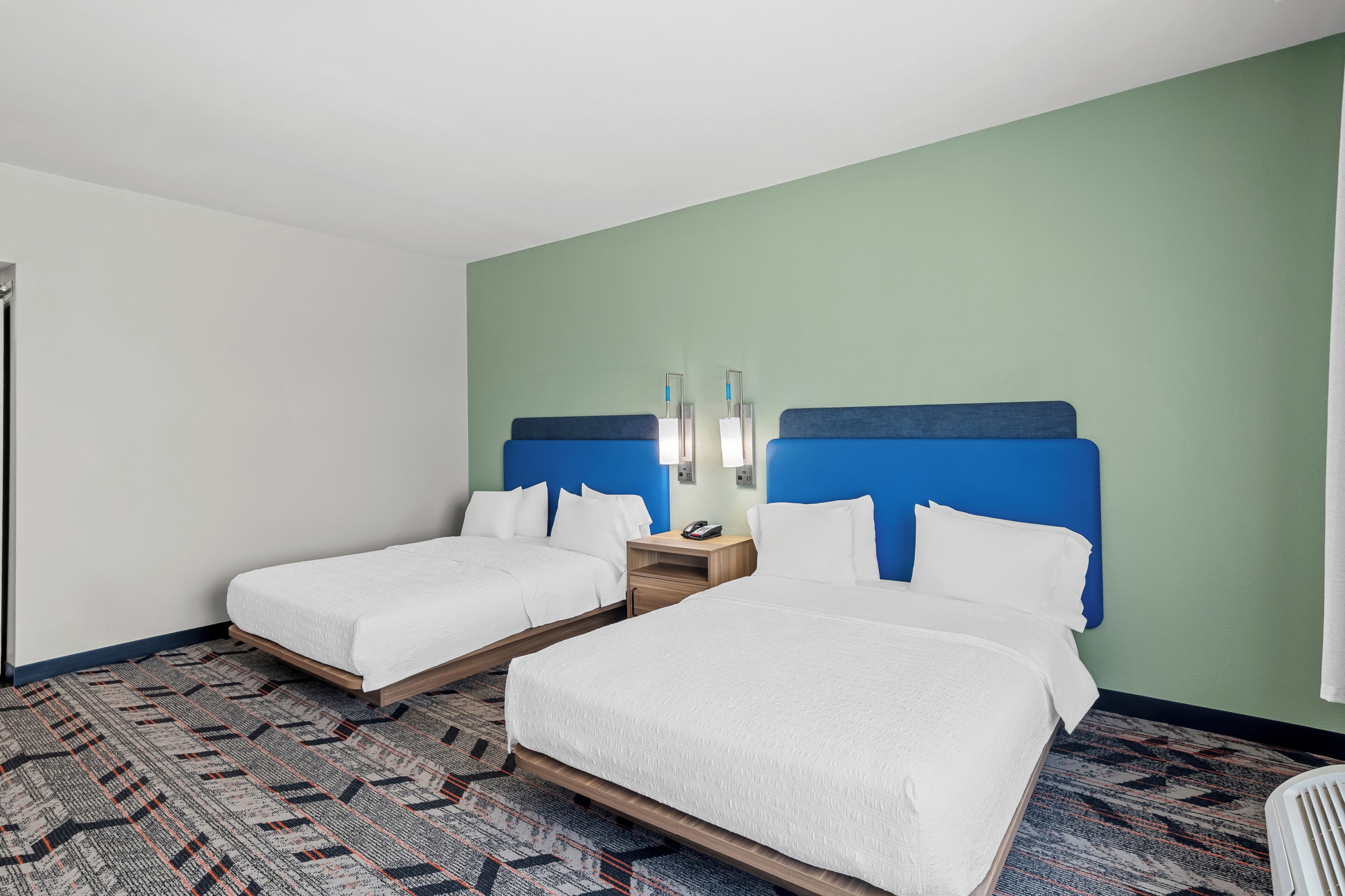 A hotel room with two beds, a patterned carpet, and a green wall.