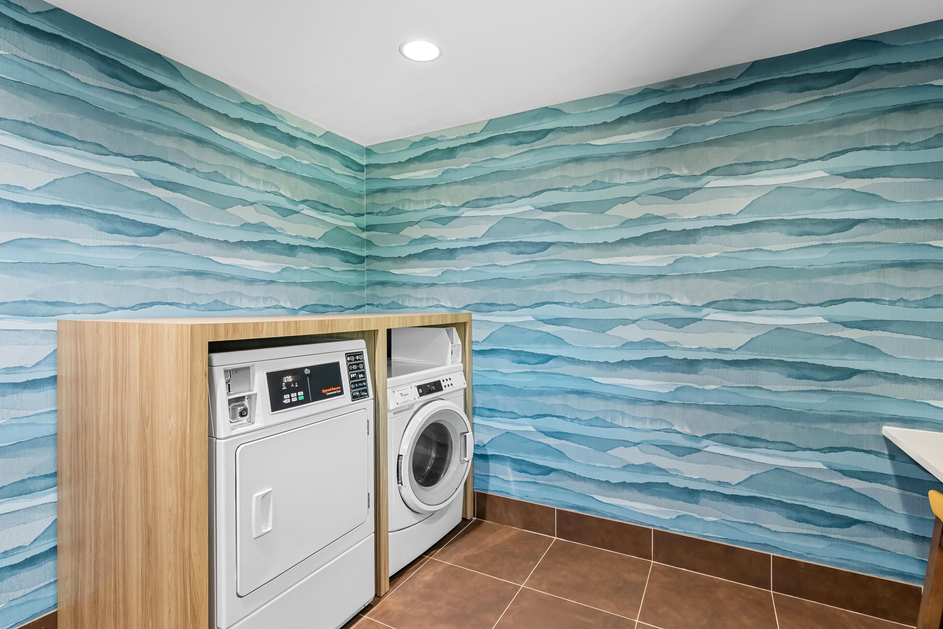 A laundry room with a washing machine and dryer, a wooden cabinet, and a wall with a blue wave pattern.