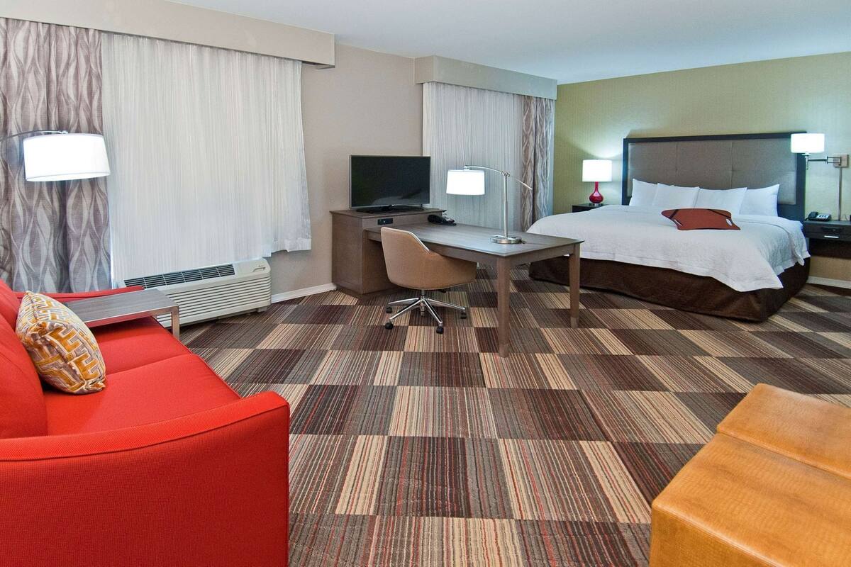 A hotel room with a bed, a desk, a chair, a television, and a red sofa.
