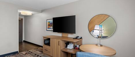Hotellihuone, jossa on televisio, peili, työpöytä ja kuviollinen matto.