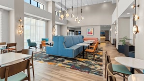 Ein modernes Interieur mit einem blauen Sofa, Holztischen und -stühlen sowie einem farbenfrohen Teppich.